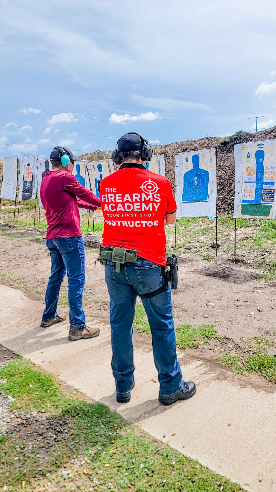 Professor Manny Galvan in a Firearms Academy instructor shirt coaching a student at an outdoor shooting range