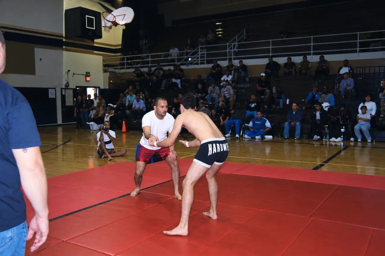 Manny Galvan in a grappling match on red mats in a school gym with spectators in the stands