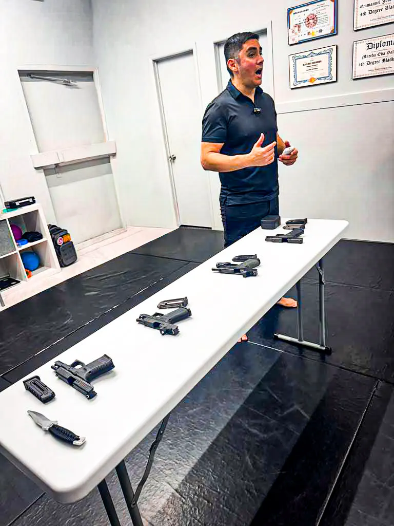 Professor Manny Galvan teaching a gun safety class beside a table of training pistols