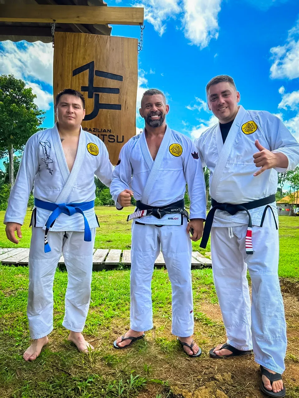 Manny Galvan in a white gi standing outdoors with Dr. Carlos Sanchez Moctezuma and Master Paulo Brandao in Brazil