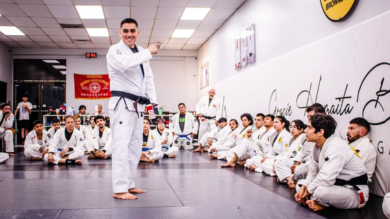 Professor Manny Galvan in a white gi leading a seminar, with rows of students in gis seated on the mat