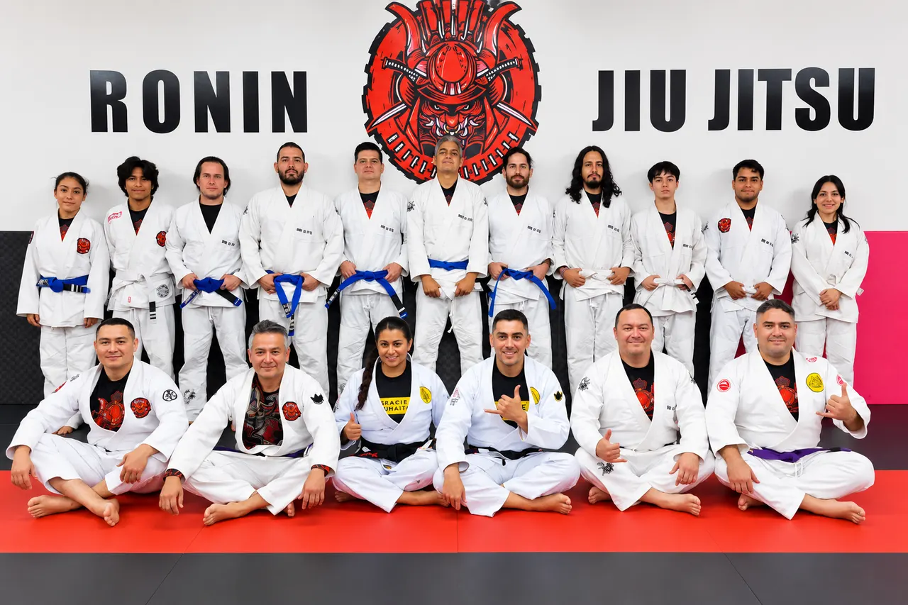 El Profesor Manny Galvan con alumnos de Ronin Jiu Jitsu Academy en Matamoros, México, frente al logotipo de la academia